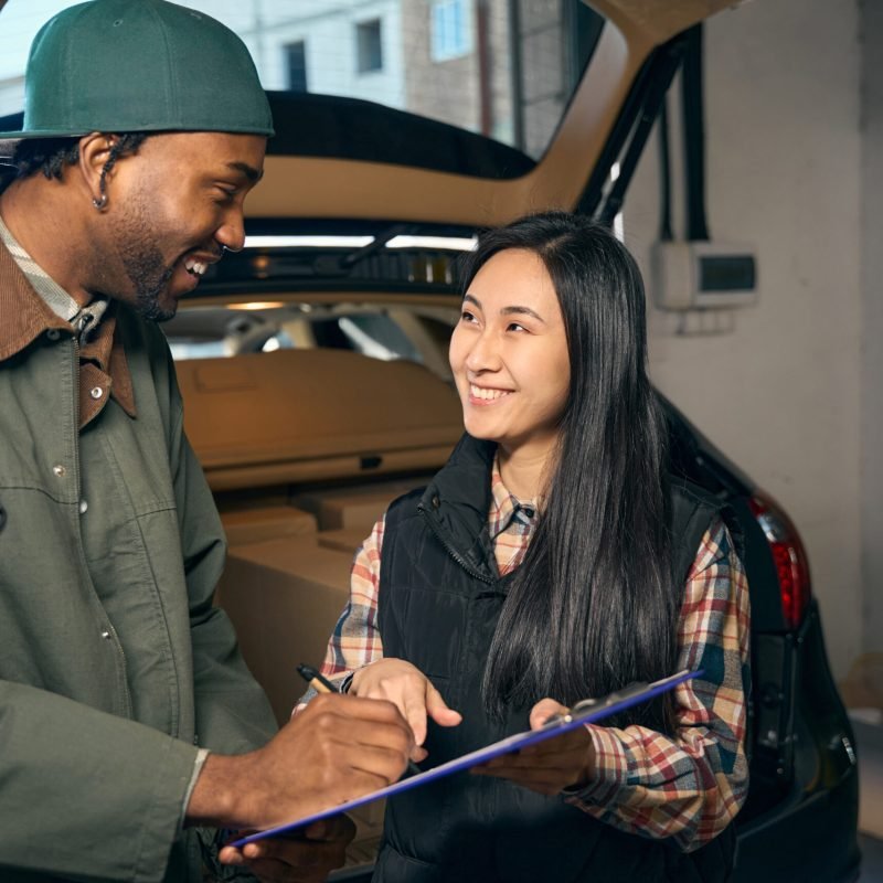 Young couple is filling out a folder while standing against the background of a car with an open trunk
